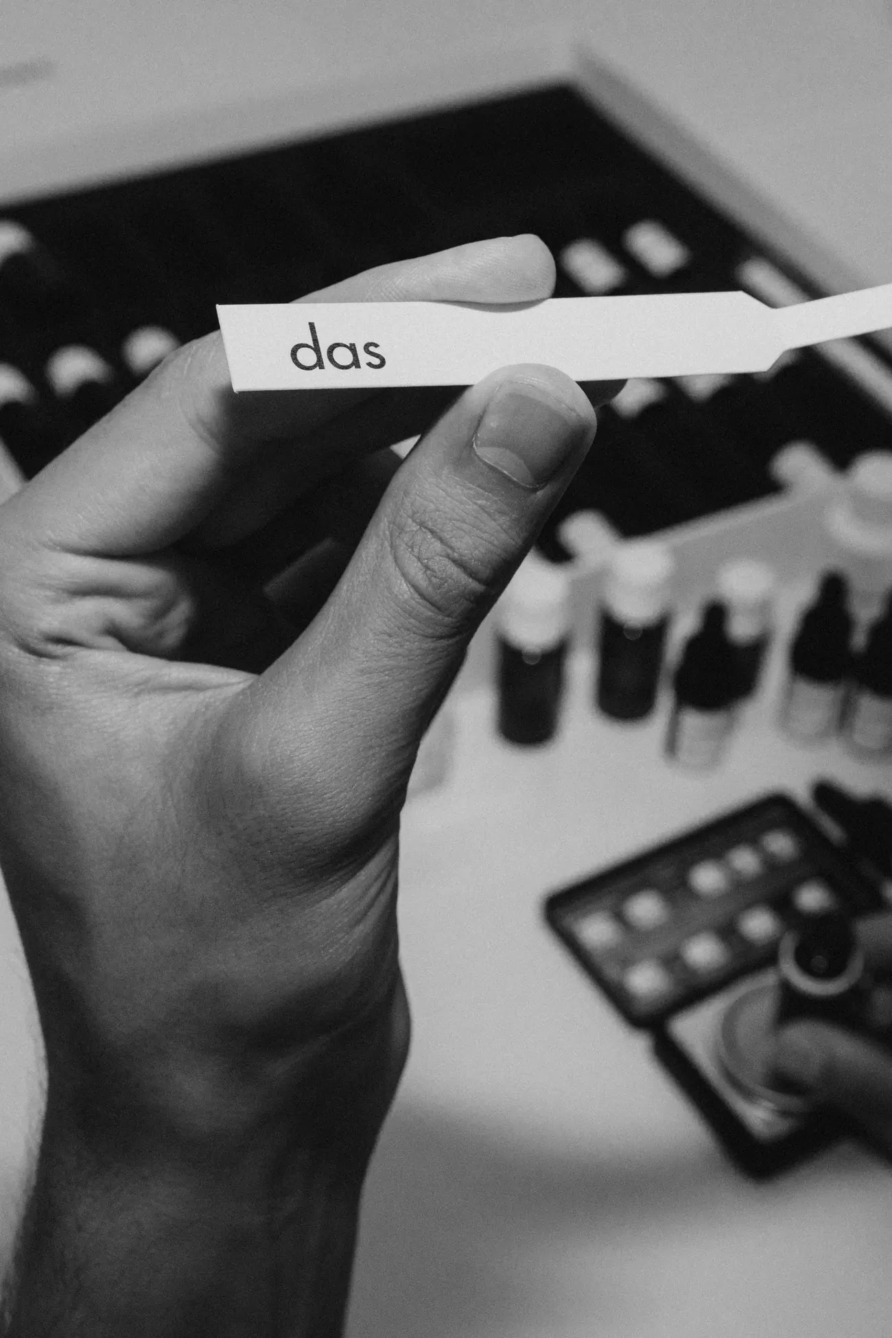 eine hand hält einen duftstreifen mit dem schriftzug das über die rohstoffflaschen