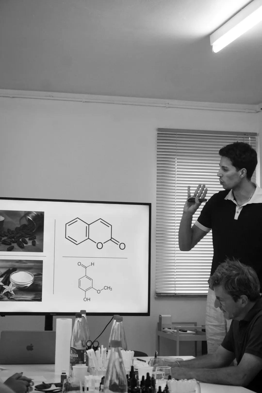 rodi erklärt vor einem bildschirm mit den molekülen von cumarin und vanillin, daneben tonkabohnen und vanille